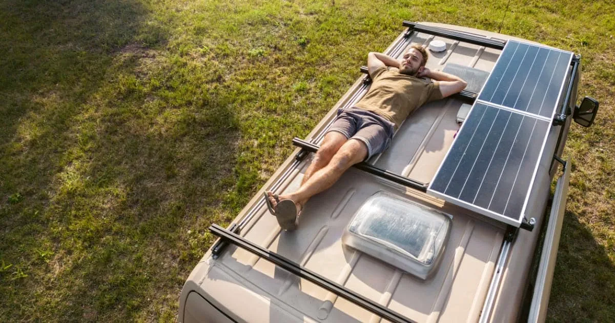 Homme allongé sur le toit d'un camping-car avec panneau solaire.
